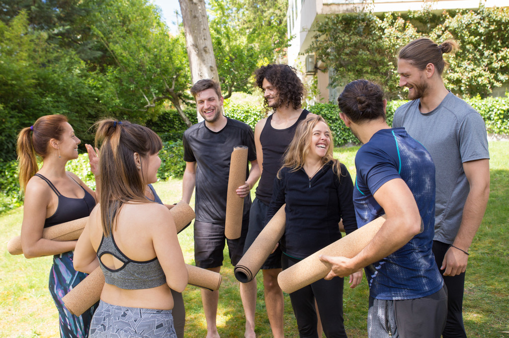 Groupe de participants souriants en tenue de sport, tapis de yoga roulés sous le bras, réunis en extérieur dans un jardin