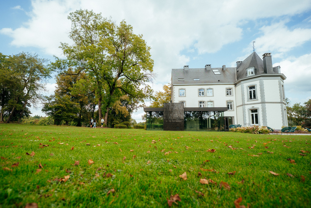 Château de la Louveterie, façade blanche et extension vitrée contemporaine, vue depuis la pelouse parsemée de feuilles d’automne