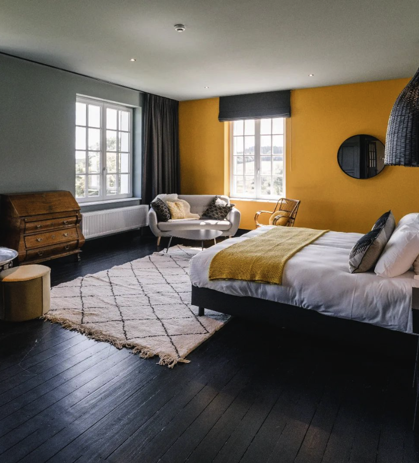 Chambre spacieuse du Domaine de Bronromme, mur ocre et parquet foncé, lit double et coin salon près des fenêtres donnant sur la campagne