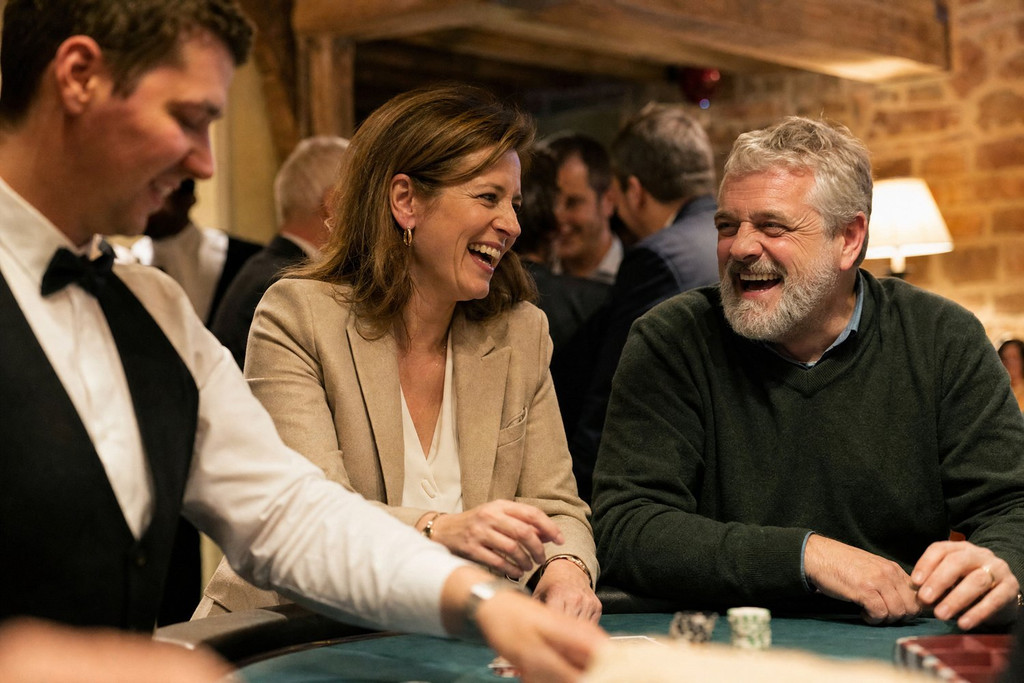 Deux collègues éclatent de rire à une table de casino, le croupier debout à leur gauche